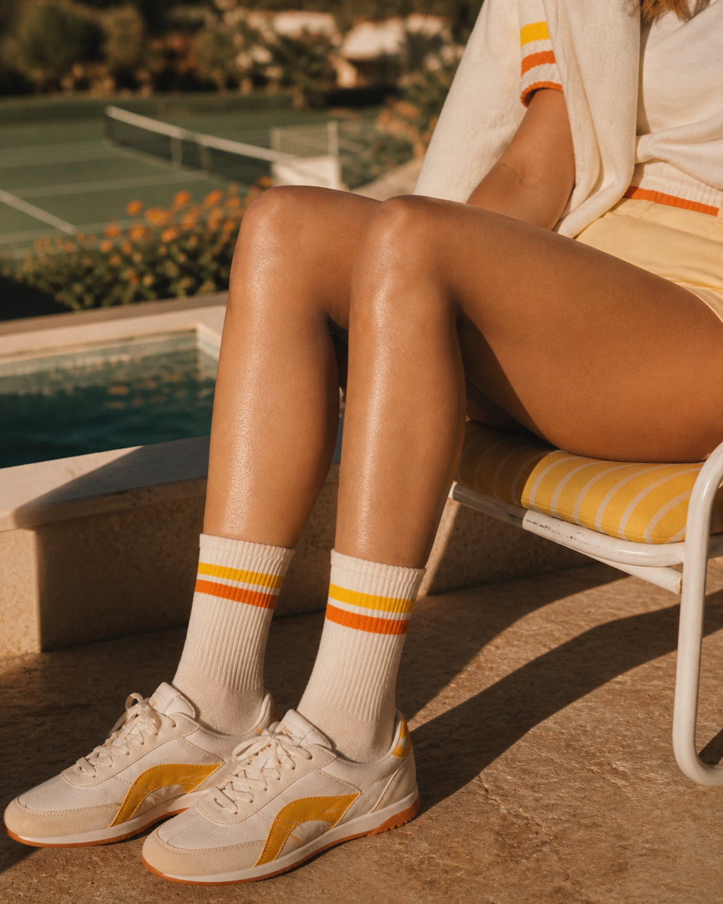 Person sitting by a pool wearing white sneakers with orange accents and striped socks.